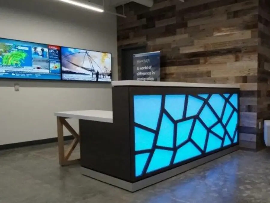 Custom reception desk with a backlit blue geometric front panel and reclaimed wood wall