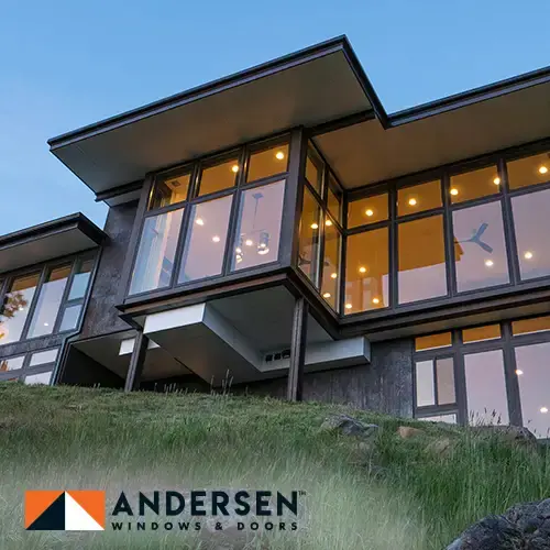 Modern hillside home with walls of dark-framed windows, with Andersen Windows & Doors logo