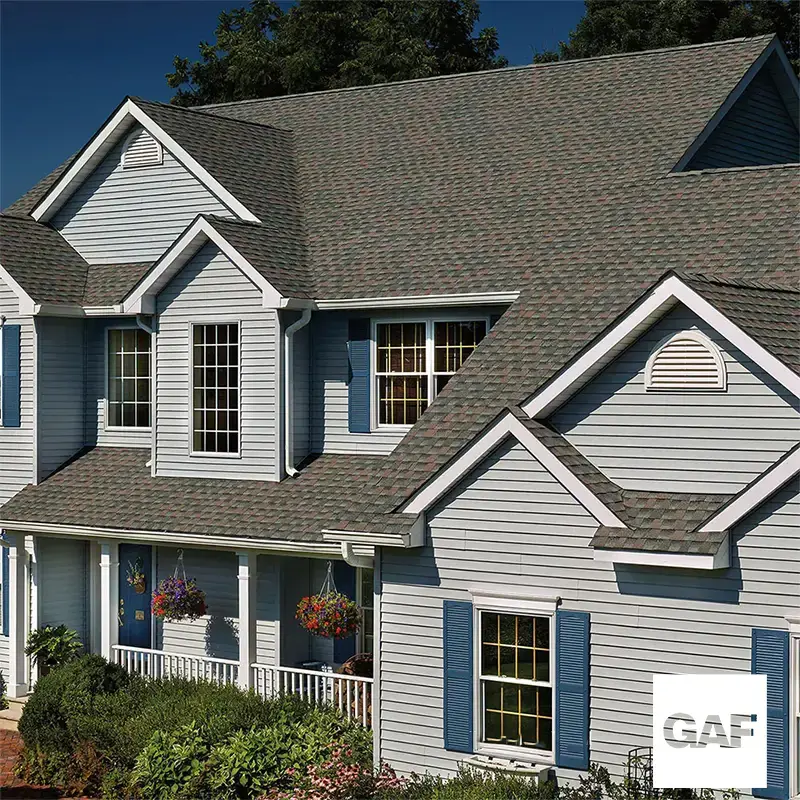 Two-story blue-gray sided home with a multi-gable shingle roof, with GAF logo