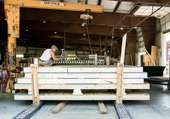 Worker assembling wood wall panels on a rack under an overhead hoist in a plant