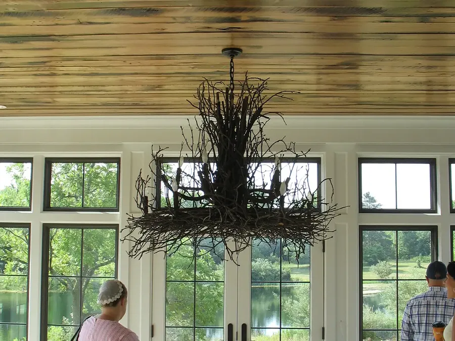 Rustic branch chandelier hanging below a plank ceiling in a room with tall windows