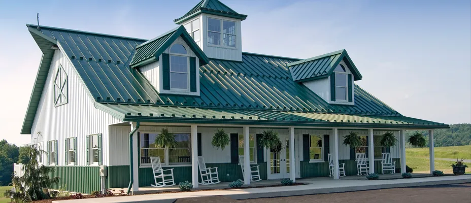 Post-frame building with green metal roof, cupola and rocking chairs on a wraparound porch