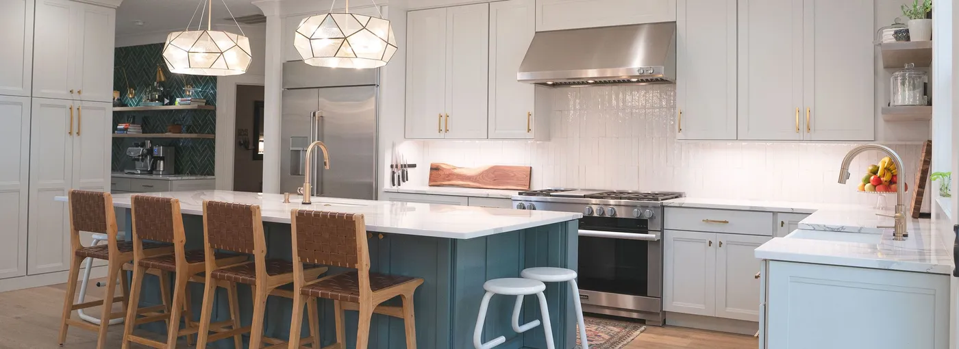 White kitchen with blue island, leather bar stools and geometric pendant lights