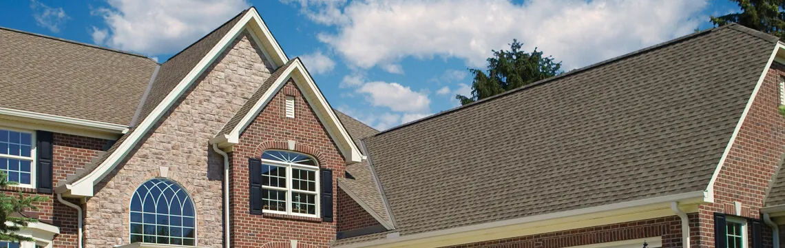 Brick and stone house with tan architectural shingle roof under a blue sky