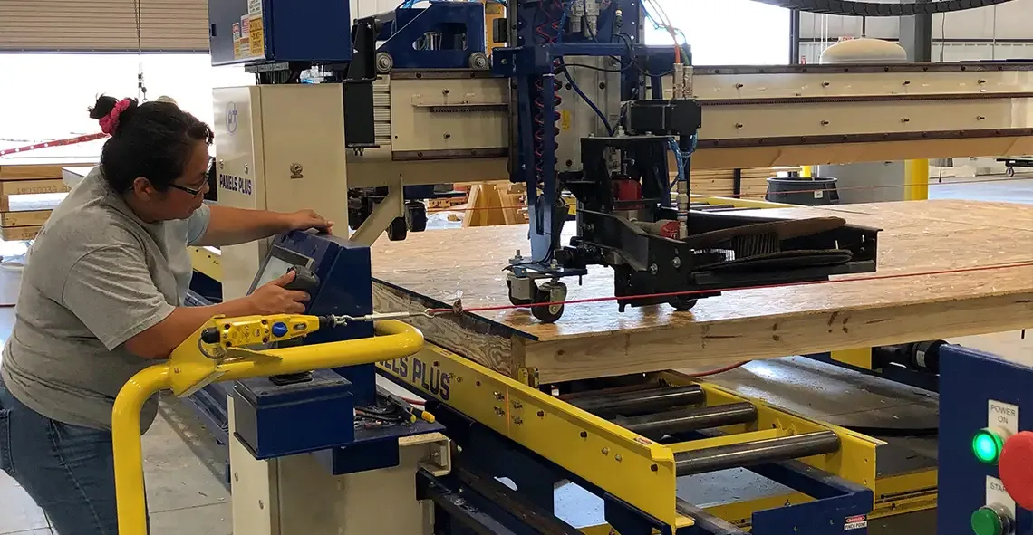 Worker operating an automated nailing machine on a wall panel in a plant